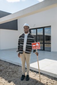 man wearing a hard hat holding a sign outside a house